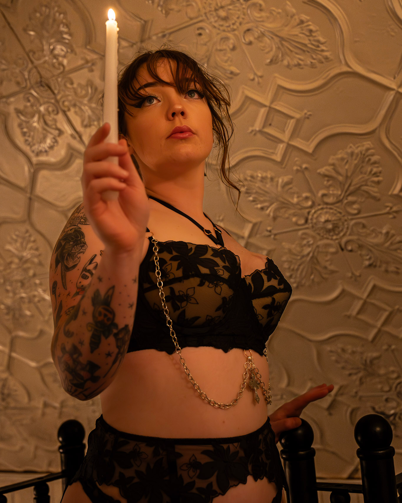 Person in lingerie holding a candle against a textured wall.