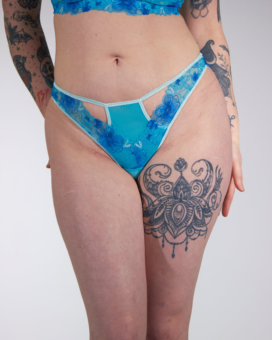 Person wearing blue patterned underwear with tattoos on arms and legs.